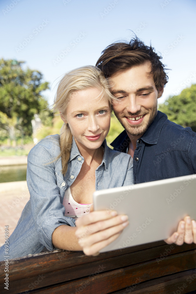 Young couple using digital tablet on park bench Young couple using digital tablet on park bench