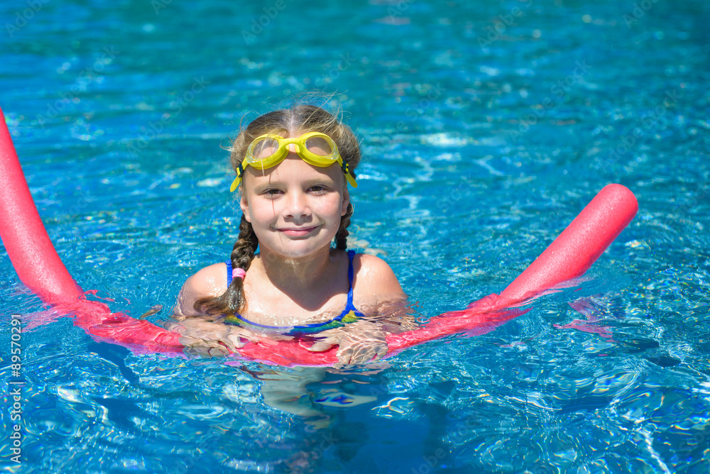 Adorable little girl swimming with a pink foam noodle in a pool