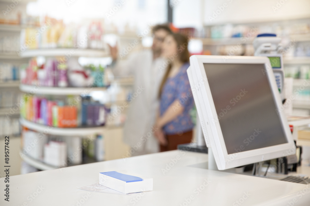 Prescription and drug lying on counter of a pharmacy while pharmacist advising female customer in the background Prescription and drug lying on counter of a pharmacy while pharmacist advising female customer in the background