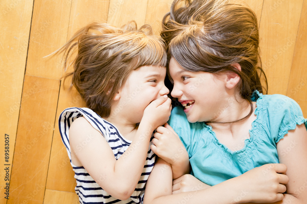 Two sisters lying face to face on wooden floor Two sisters lying face to face on wooden floor