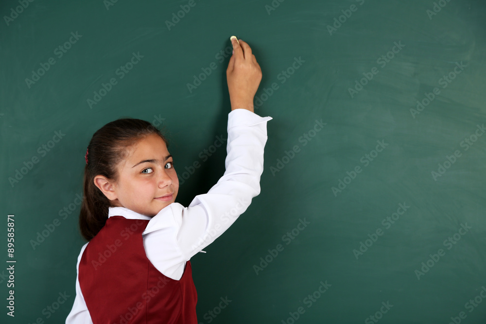 Beautiful little girl writes on blackboard in classroom