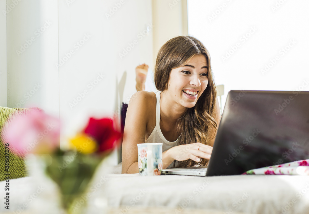 Relaxed young woman lying in bed using laptop Relaxed young woman lying in bed using laptop