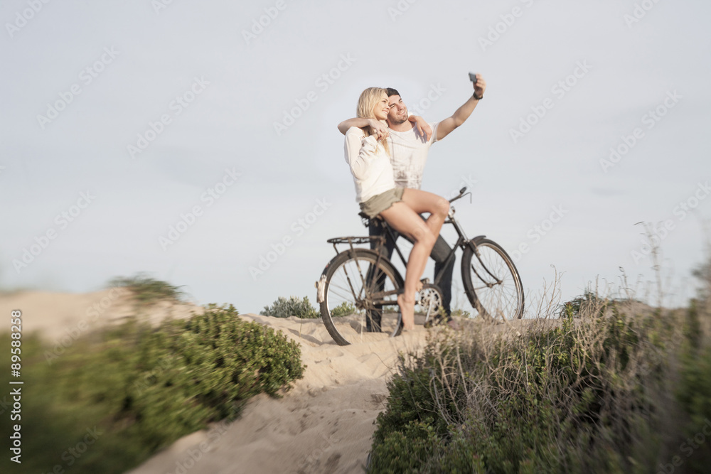Young couple with bicycle taking a selfie on a beach dune Young couple with bicycle taking a selfie on a beach dune