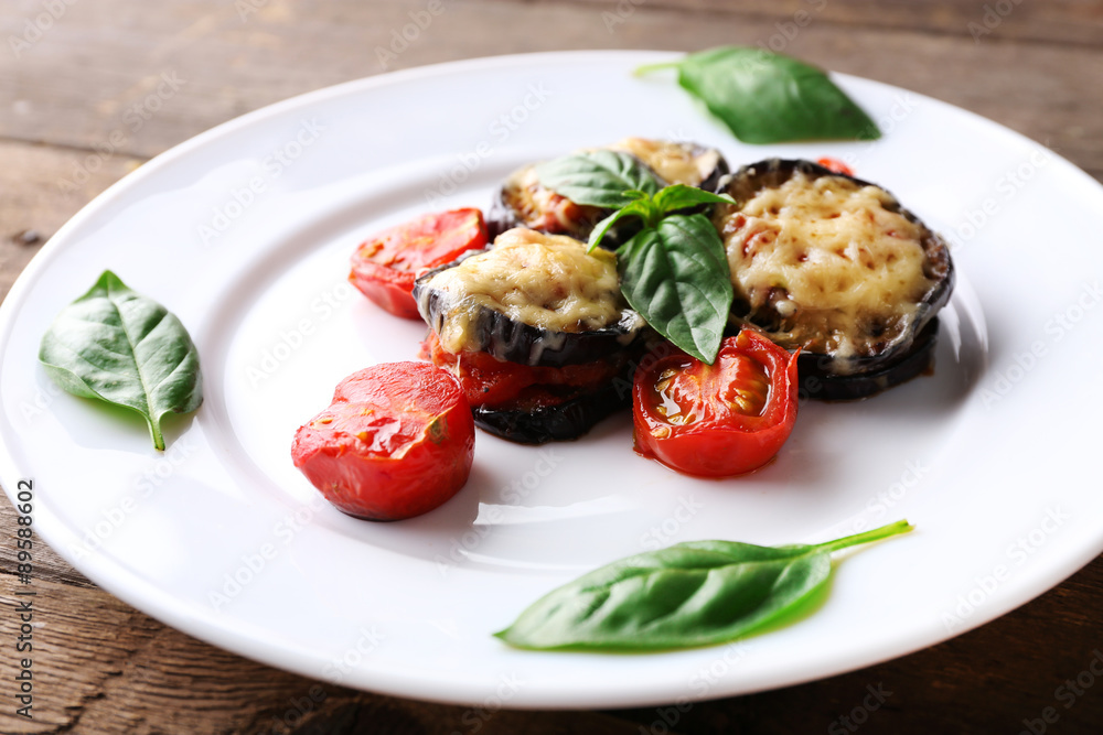 Dish of eggplant with cherry tomatoes and cheese in white plate on wooden table, closeup Dish of eggplant with cherry tomatoes and cheese in white plate on wooden table, closeup