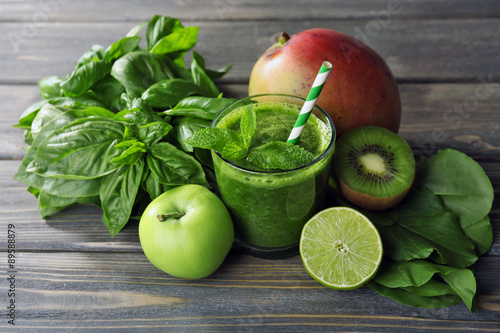 Green healthy juice with fruits and herbs on wooden table close up