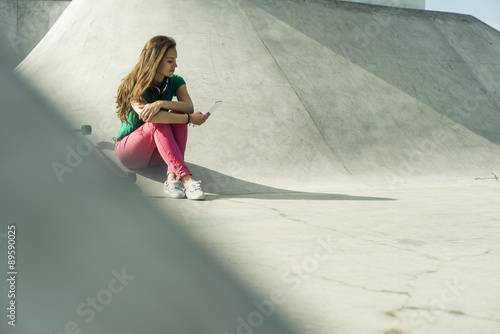 Young skate boarder sitting in a skatepark using smartphone