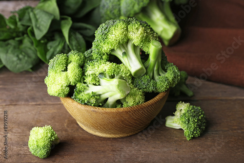 Fresh broccoli with spinach in bowl on wooden table close up