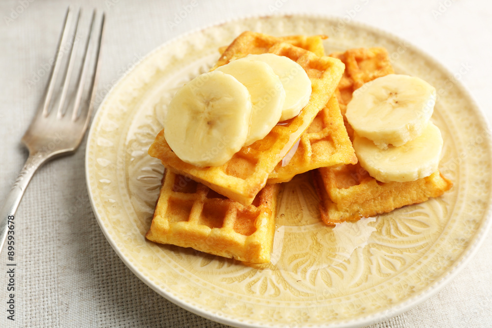 Sweet homemade waffles with sliced banana on plate, on light background Sweet homemade waffles with sliced banana on plate, on light background