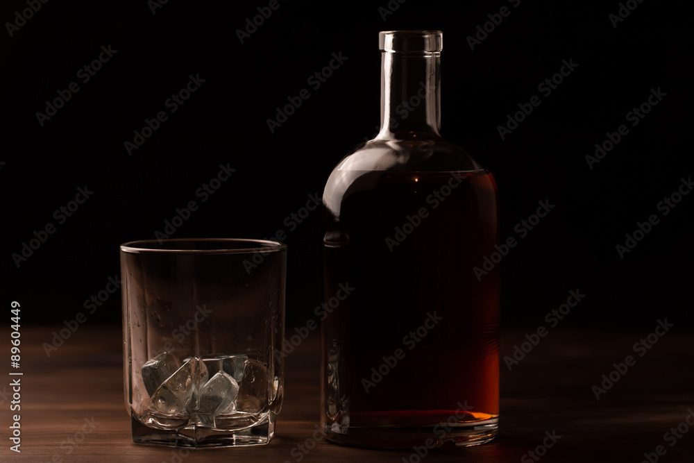 glass of whiskey with ice and a bottle on a wooden table. Cognac, brandy. glass of whiskey with ice and a bottle on a wooden table. Cognac, brandy.
