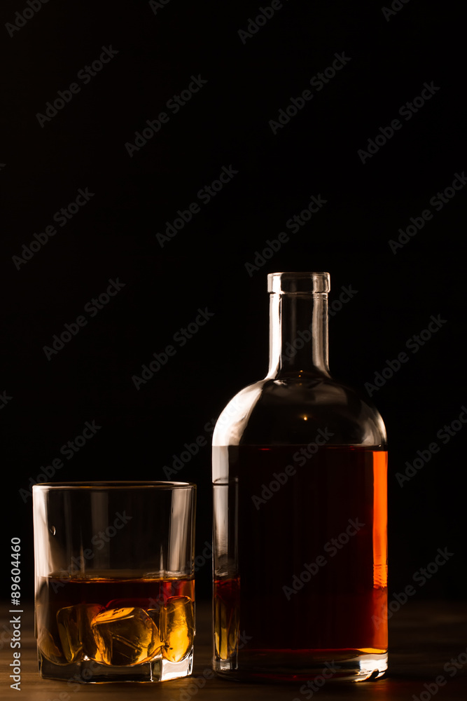 glass of whiskey with ice and a bottle on a wooden table. Cognac, brandy. glass of whiskey with ice and a bottle on a wooden table. Cognac, brandy.