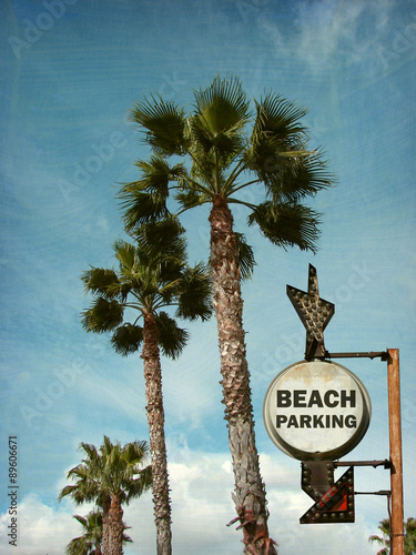 aged and worn vintage photo of beach parking sign with palm trees