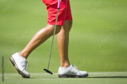 Female golfers walking on green with putter.