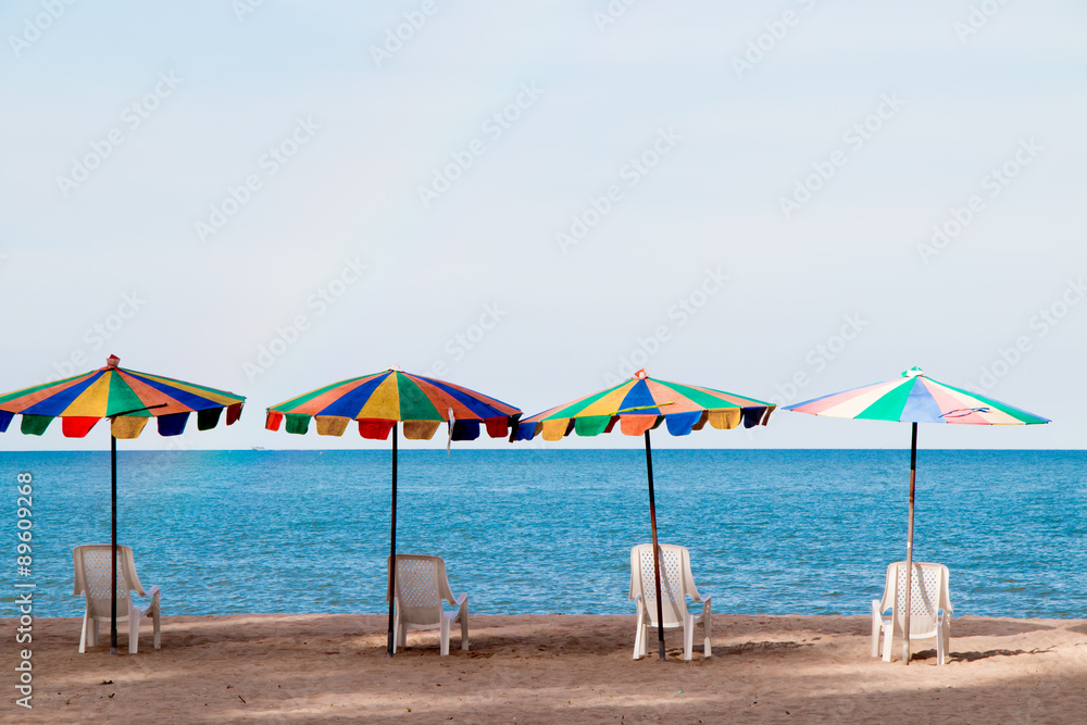 Fototapeta premium Beach chairs with colorful umbrella at the beach with blue-sky background on summer.