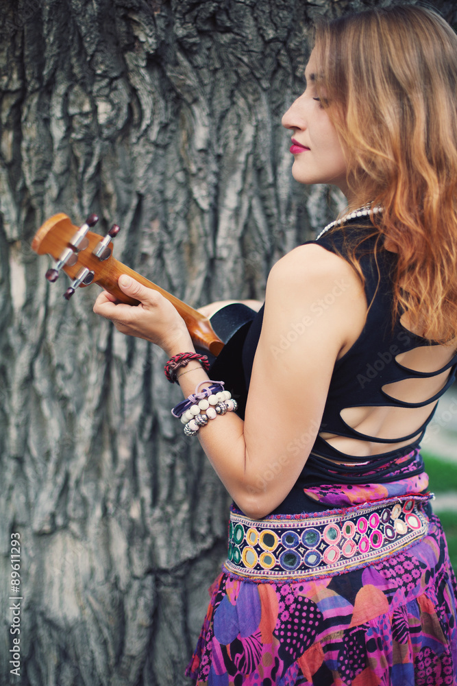 Obraz premium Young Lady Hippie Girl with Red Hair Playing Music on Ukulele Small Guitar Outdoor