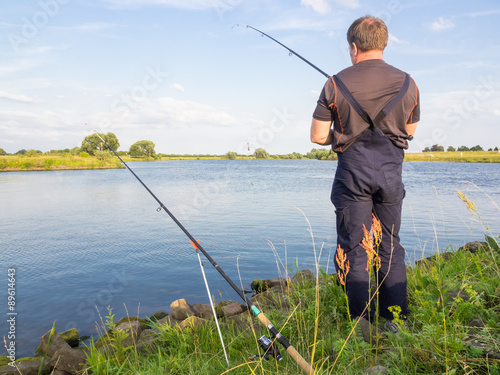 Männlicher Angler steht am Fluss bei blauem Himmel