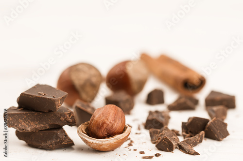 Broken chocolate bar, hazelnut and cinnamon on wooden background, close-up