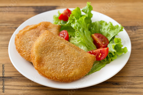portuguese meat cookies with fresh salad on white dish on brown wooden background