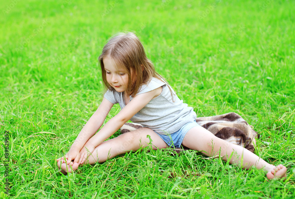 Fototapeta premium Little girl child sitting on the grass does yoga stretching exer