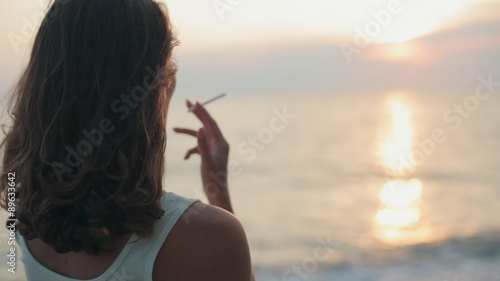 Beautiful woman smoking a cigarette at sunset near the sea