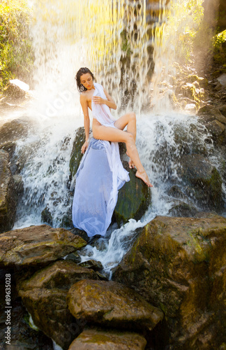 Fototapeta Naklejka Na Ścianę i Meble -  Naked girl sitting on a rock by a waterfall.