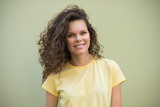 Attractive young girl with brown curly hair standing in a yellow