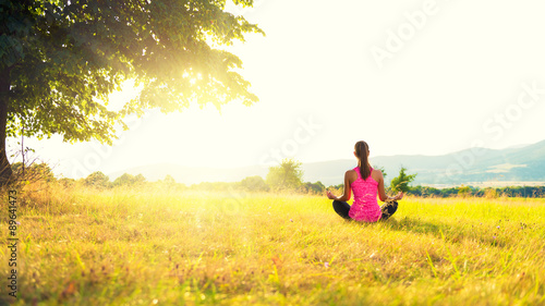 Young athletic woman practicing yoga on a meadow at sunset  image with lens flare