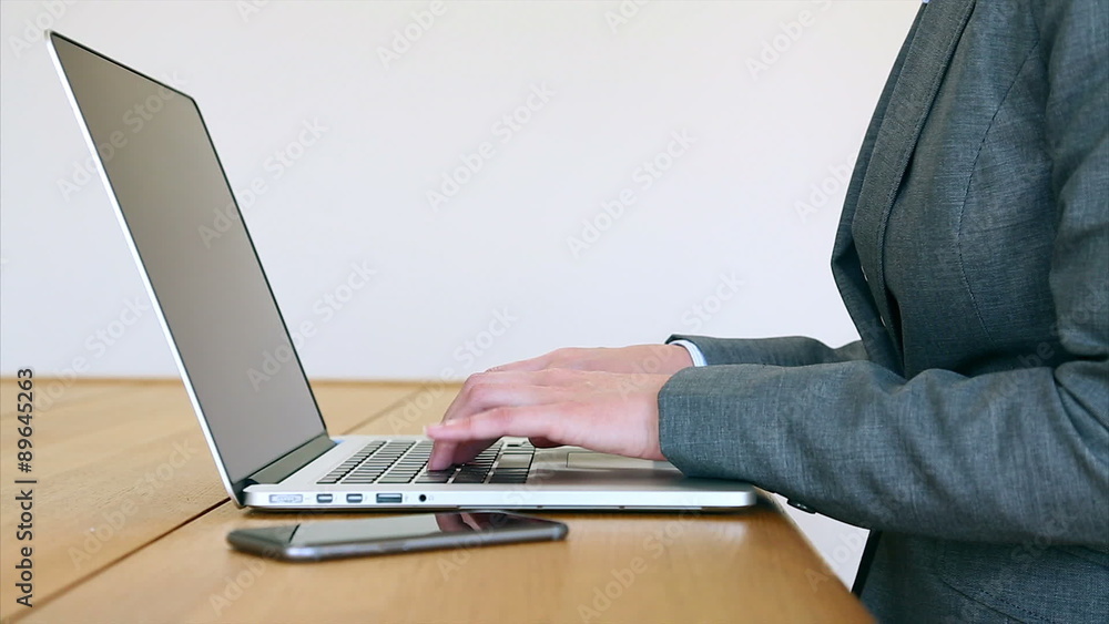 Locked down shot of female executive using laptop and smart phone. Businesswoman is sitting at wooden desk. She is multitasking in office. Locked down shot of female executive using laptop and smart phone. Businesswoman is sitting at wooden desk. She is multitasking in office.