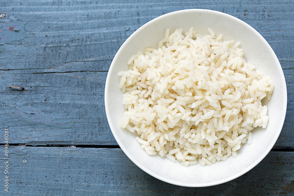 Boiled rice in a white china bowl on rustic blue wood Boiled rice in a white china bowl on rustic blue wood