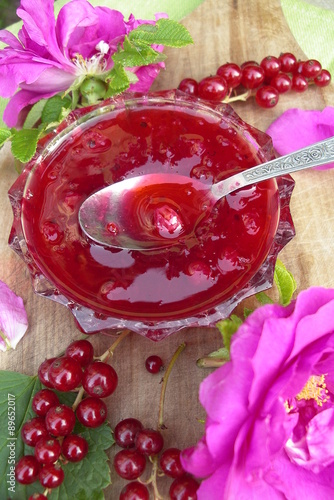 Socket with red currant jam with rose petals on the board with berries red currant and roses