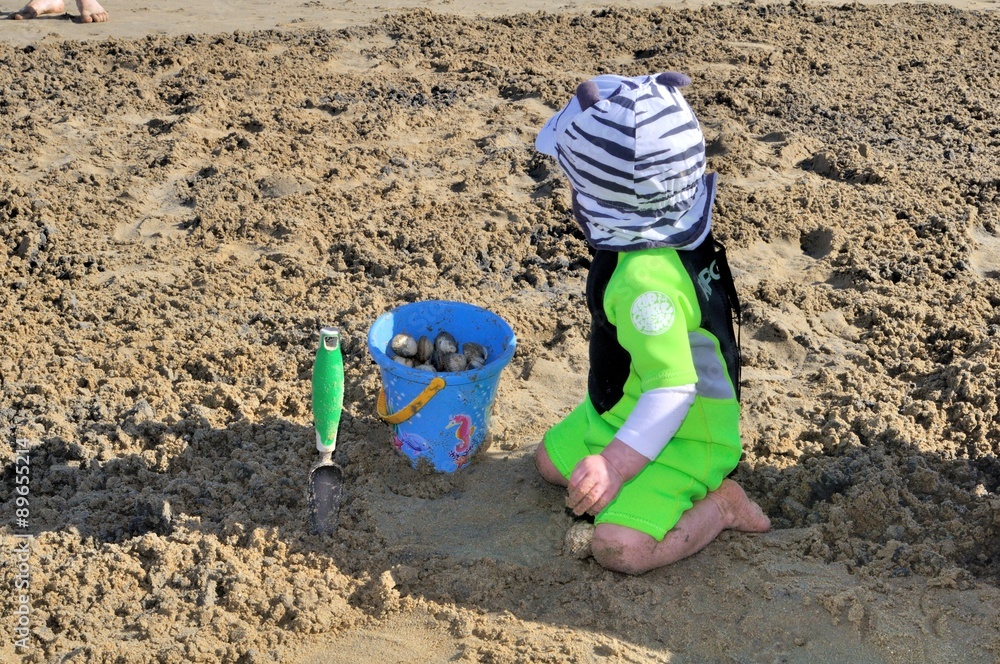 Jeune enfant ramassant des coquillages sur le sable à la mer Jeune enfant ramassant des coquillages sur le sable à la mer