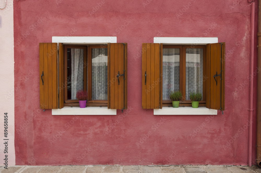 Two windows on a red wall from a colorful house of Burano island