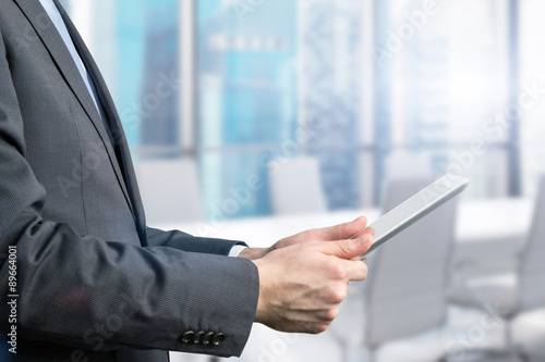 Close-up of side view of a businessman who is browsing on his tablet. Office view with Singapore panoramic view.
