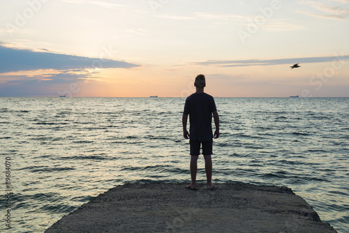 Young man observes sea sunrise horizon, back view