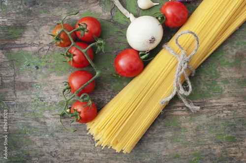 Pasta spaghetti, onion, garlic and tomato on wooden background