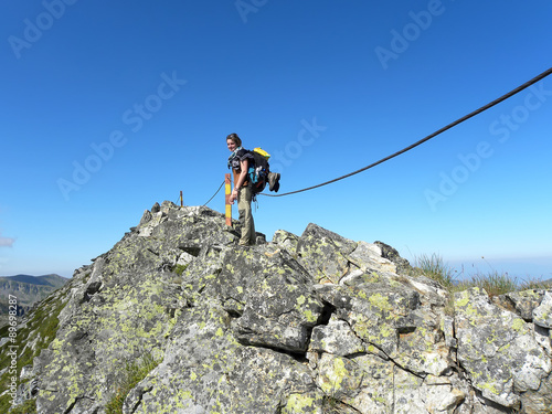 Young girl by the rope on steep stony mountain peak