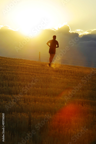 Silhouette sport man running off road in countryside on yellow grass field at sunset