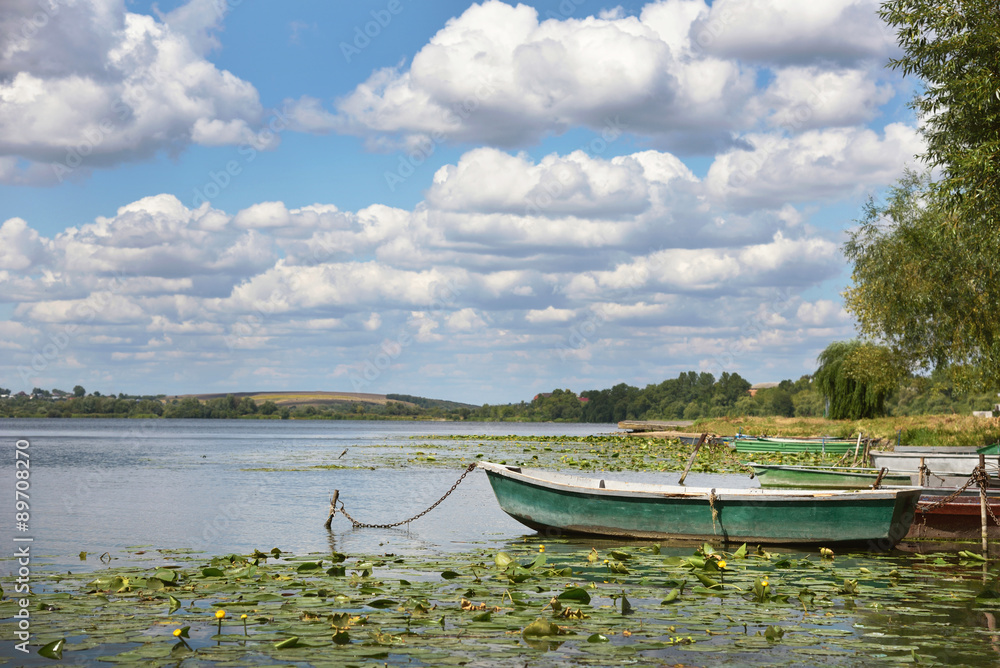 The charming landscape of lonely boat on the pond on a backgroun The charming landscape of lonely boat on the pond on a backgroun