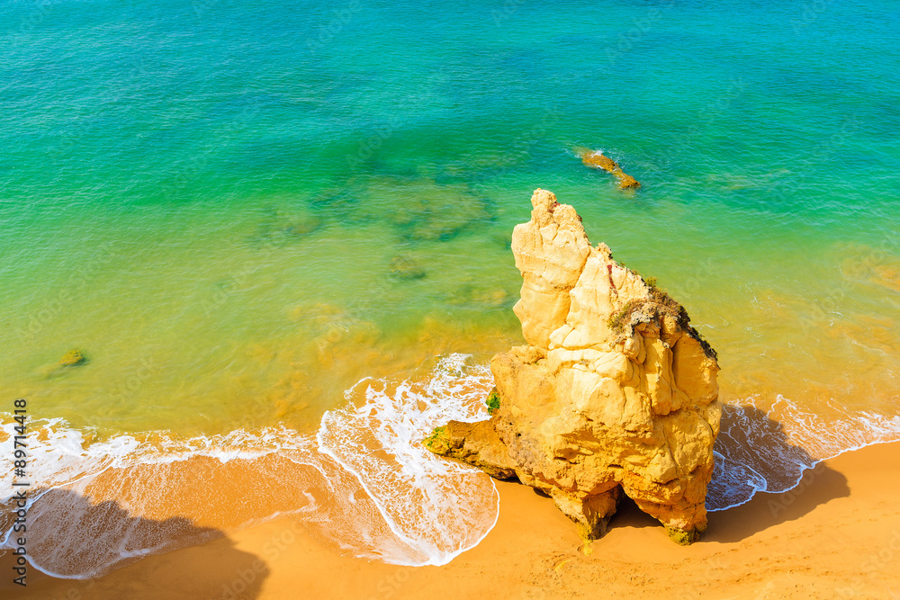 Rock on sandy Praia da Rocha beach in Portimao and view of turquoise sea water, Portugal