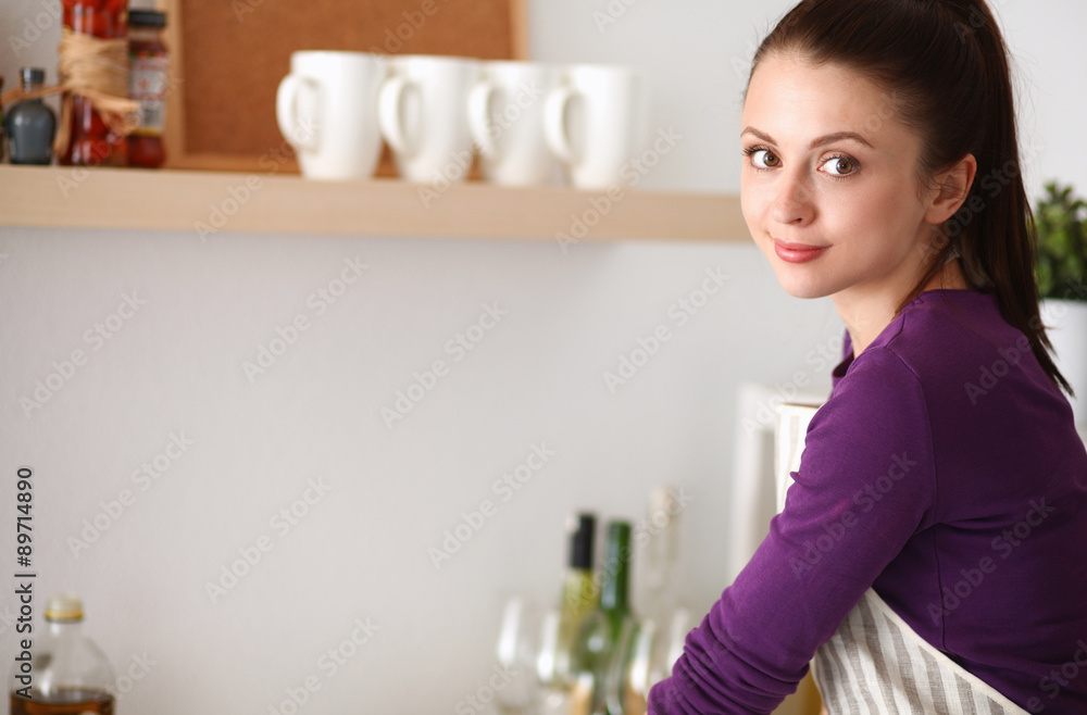Young woman standing in her kitchen near desk Young woman standing in her kitchen near desk