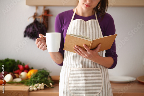 Young woman reading cookbook in the kitchen, looking for recipe photo