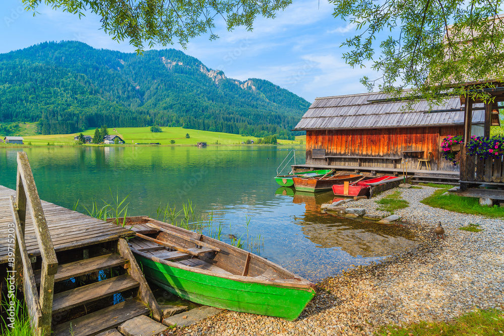 Fishing boats and wooden houses on shore of Weissensee lake in summer landscape of Carinthia land, Austria Fishing boats and wooden houses on shore of Weissensee lake in summer landscape of Carinthia land, Austria