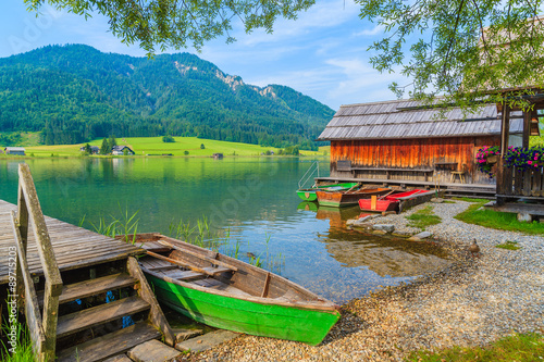 Fishing boats and wooden houses on shore of Weissensee lake in summer landscape of Carinthia land, Austria #89715203