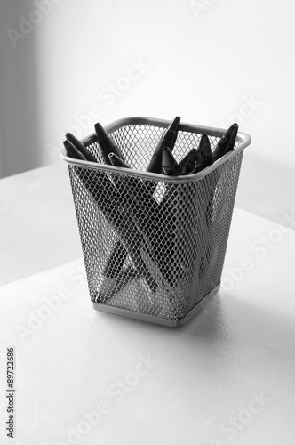 Cubilete cuadrado con bolígrafos en un escritorio en blanco y negro photo