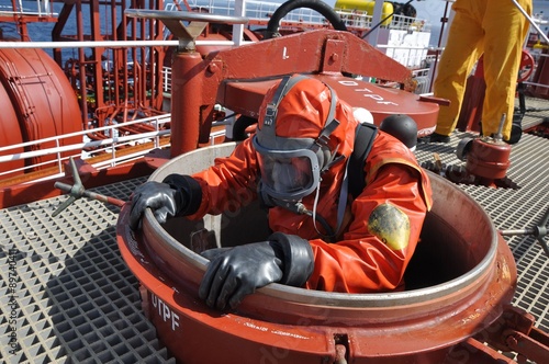 man in chemical suit entering inside cargo tank on deck of chemical tanker for cleaning operation