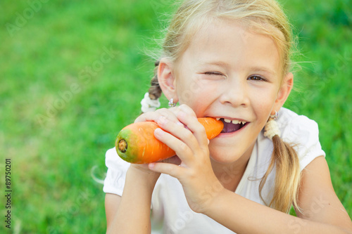 Photos Happy little girl eating carrot at the day time.