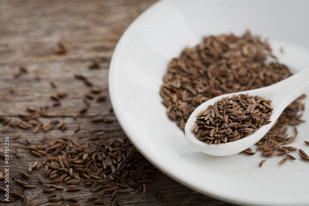 Cumin seeds or caraway in white spoon on wooden board Cumin seeds or caraway in white spoon on wooden board