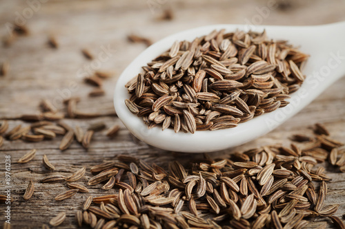 Cumin seeds or caraway in white spoon on wooden board