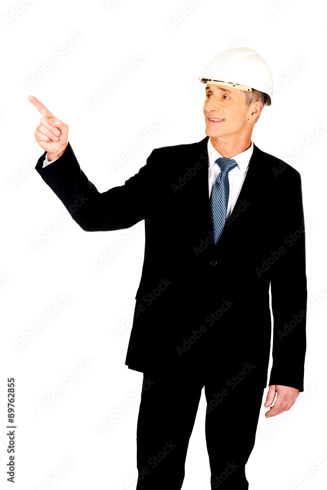 Smiling businessman with hard hat pointing up