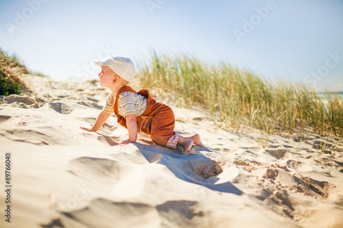 Cute toddler climing up on a sandy hill on the beach