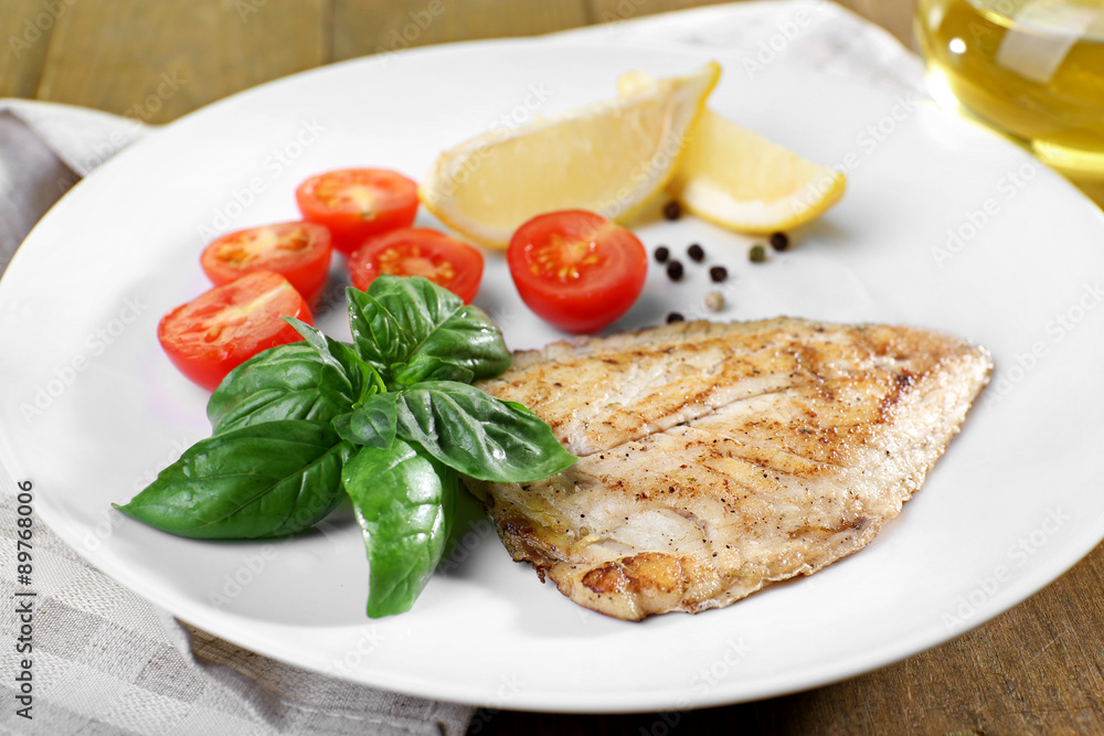 Dish of fish fillet with basil and lemon on plate close up Dish of fish fillet with basil and lemon on plate close up